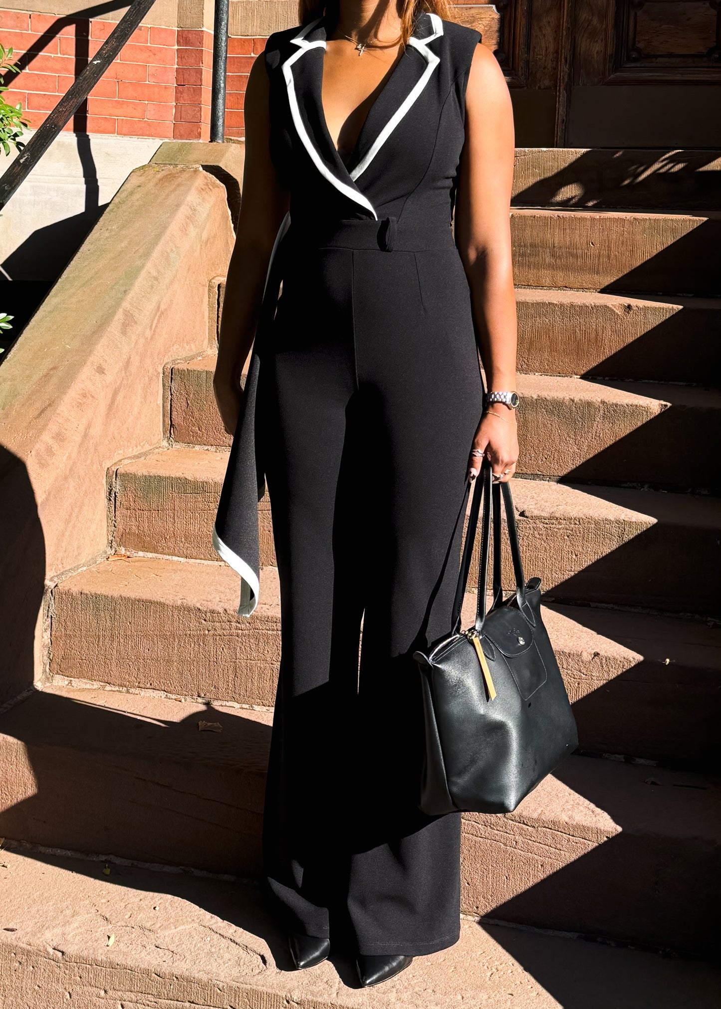 Person wearing a black jumpsuit with white trim, standing on steps outdoors.